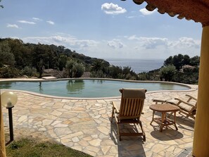 A pool with a stone patio, a wooden chair, and a table. - Villa with a pool and a view of the sea (Torre Delle Stelle (Maracalagonis))