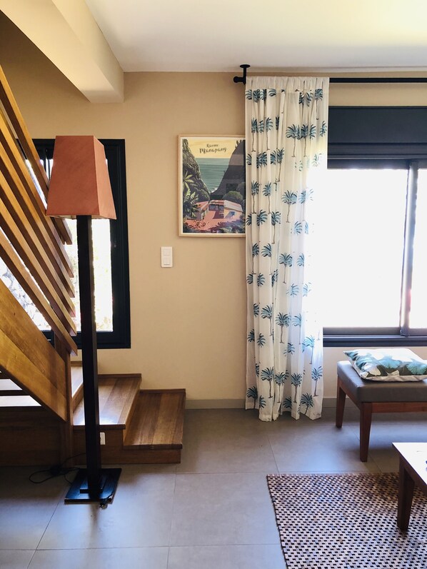 A room with a wooden staircase, a standing lamp, a framed picture on the wall, a window with curtains, and a small table with a cushion. - SAINT GILLES LES BAINS, Waterfront, seaside Maison BALEINES, 4 **** (Saint Paul)