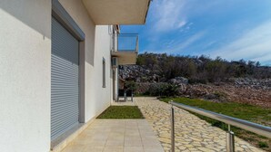 Ein modernes Gebäude mit geschlossenem Garagentor, einem Balkon und einem steinernen Weg, der zu einer felsigen Landschaft führt.