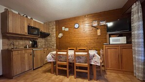A compact kitchen with wooden cabinets, a microwave, a clock, and a dining table with chairs. - 2-room apartment near slopes with balcony (La Chapelle-d'Abondance)
