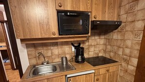 A compact kitchen with wooden cabinets, a stainless steel sink, a black coffee maker, a microwave, and a black range hood. - 2-room apartment near slopes with balcony (La Chapelle-d'Abondance)