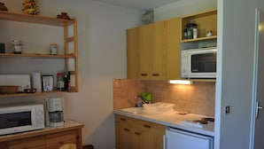 Cozinha compacta com armários de madeira, micro-ondas, cafeteira e pia.