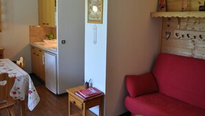 Um espaço de estar compacto com cozinha compacta, área de jantar com mesa e cadeiras, e um sofá vermelho.