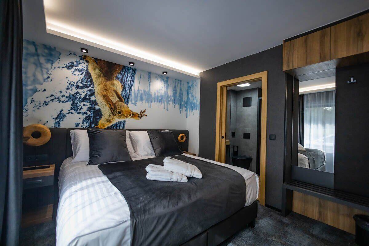 Una habitació d'hotel moderna amb un llit gran, un mural a la paret, un panell de fusta al capçal i un mirall ampli.