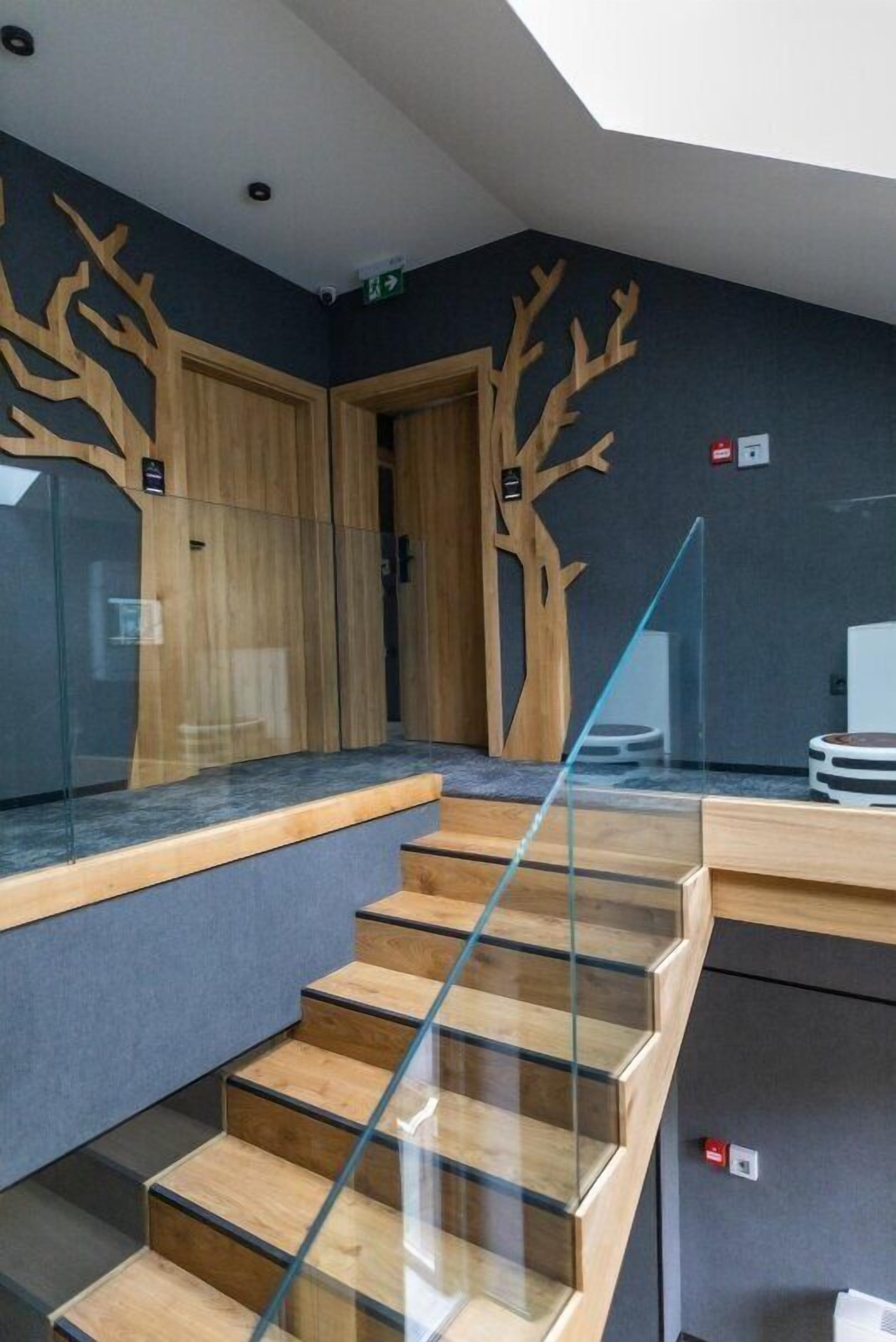A modern staircase with glass railings and wooden steps, leading to a dark room with wooden wall decor.