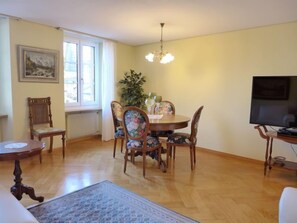 Uma sala de jantar com mesa de madeira, cadeiras florais, um lustre e uma televisão.