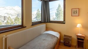 A bedroom with a bed, a radiator, a window with a view of mountains, and a lamp on a nightstand. - Les Roches Rouges (Lavachet) by Interhome (Tignes)