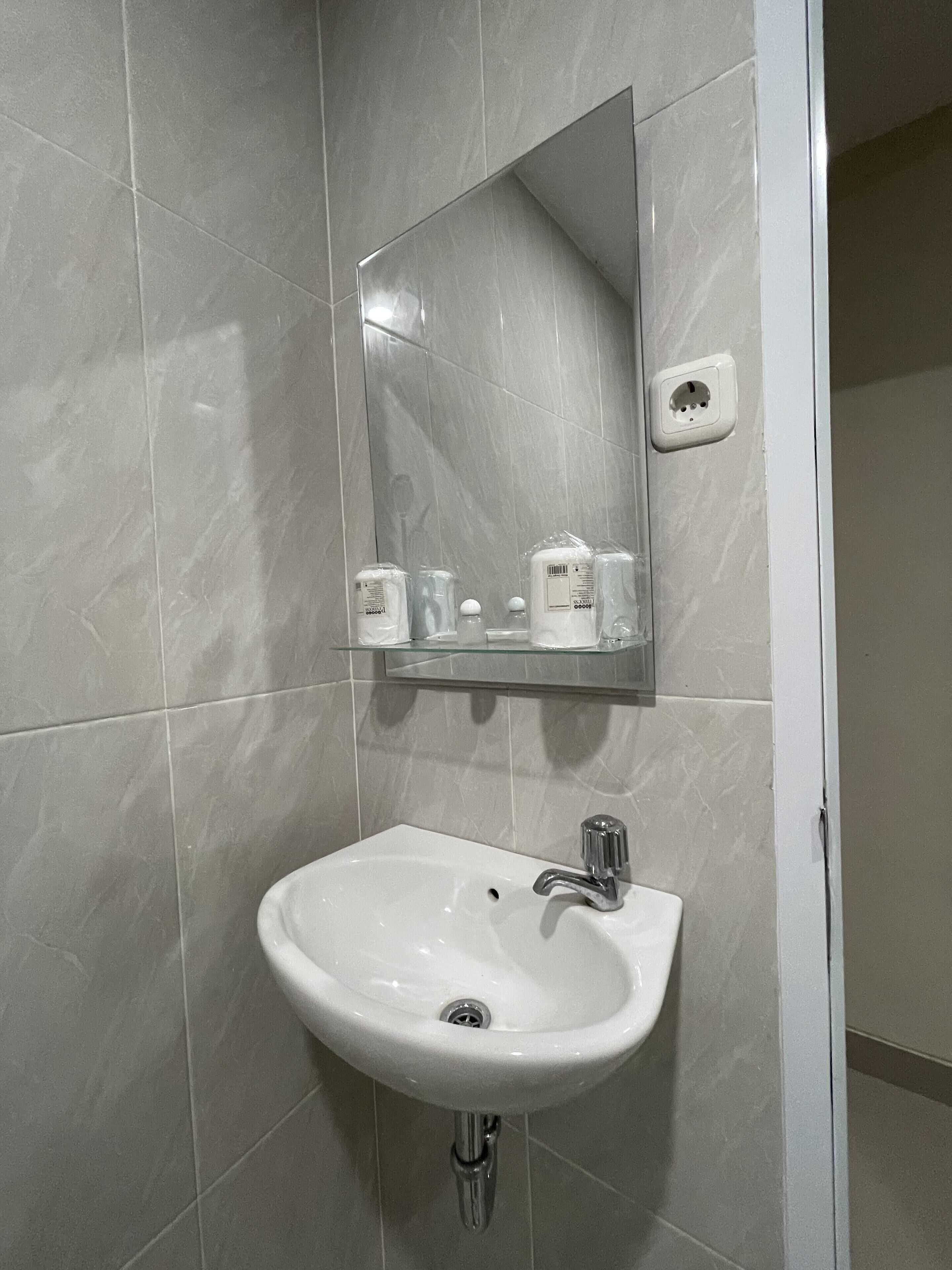Une salle de bain avec un lavabo blanc, un miroir et une étagère en verre où sont rangés les articles de toilette.