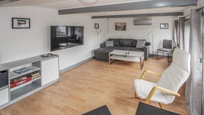 Una sala de estar moderna con un sofá gris, un sillón blanco, una mesa de centro y un televisor montado en la pared.