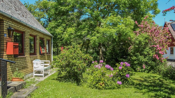 Una casa con fachada de ladrillo, un pequeño porche y un jardín con flores en flor y un árbol grande.
