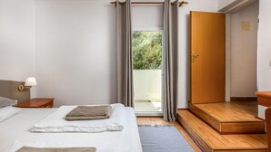 A bedroom with a bed, a nightstand, a lamp, a wooden door, and a view of the outdoors.