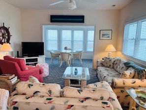 A living room with a television, red and beige sofas, a coffee table, wicker chairs, and a large window with blinds.