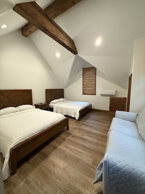 A bedroom with two beds, wooden beams, a ceiling fan, and a wall-mounted air conditioning unit.