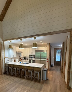 A kitchen with a large island, bar stools, stainless steel appliances, and pendant lighting. - Luxury river home on the Chattahoochee River (Demorest)