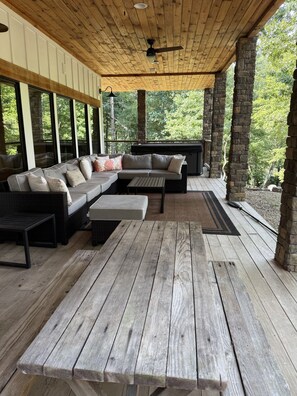 A covered outdoor seating area with a wooden ceiling, stone pillars, and a view of trees.