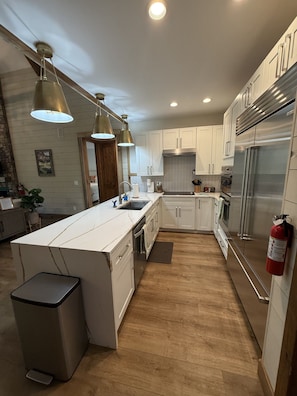 A modern kitchen with white cabinets, stainless steel appliances, pendant lighting, and a wooden floor. - Luxury river home on the Chattahoochee River (Demorest)