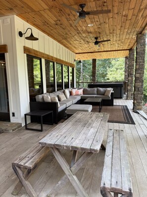 A covered outdoor seating area with a wooden ceiling, large windows, and a stone wall.