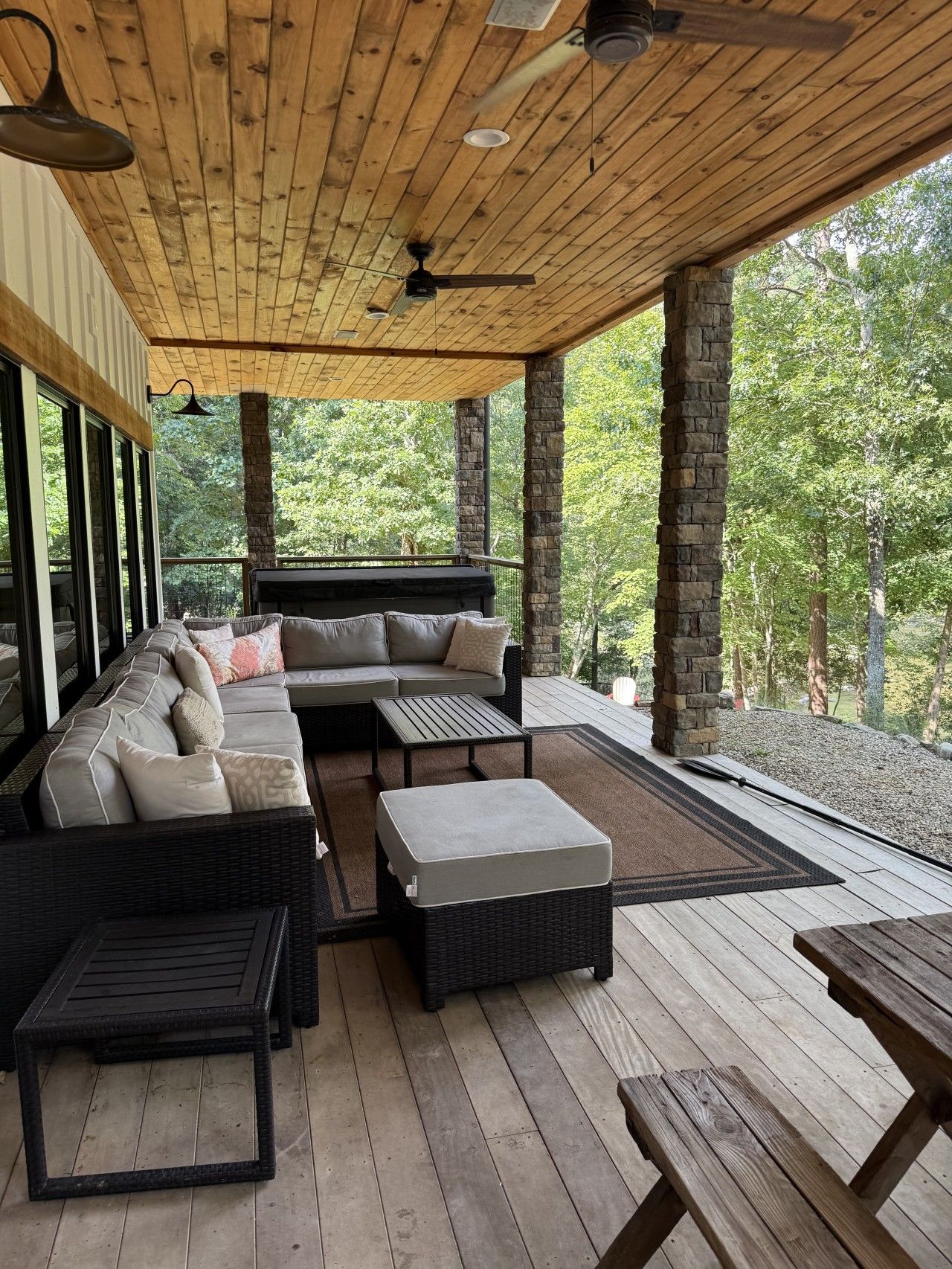 An outdoor patio with a sofa, ottoman, and tables, surrounded by stone pillars and wooden decking.