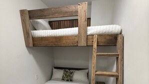 Ein Stockbett mit einer Holzleiter, weißer Bettwäsche und einem Kopfkissen mit Blattmuster.