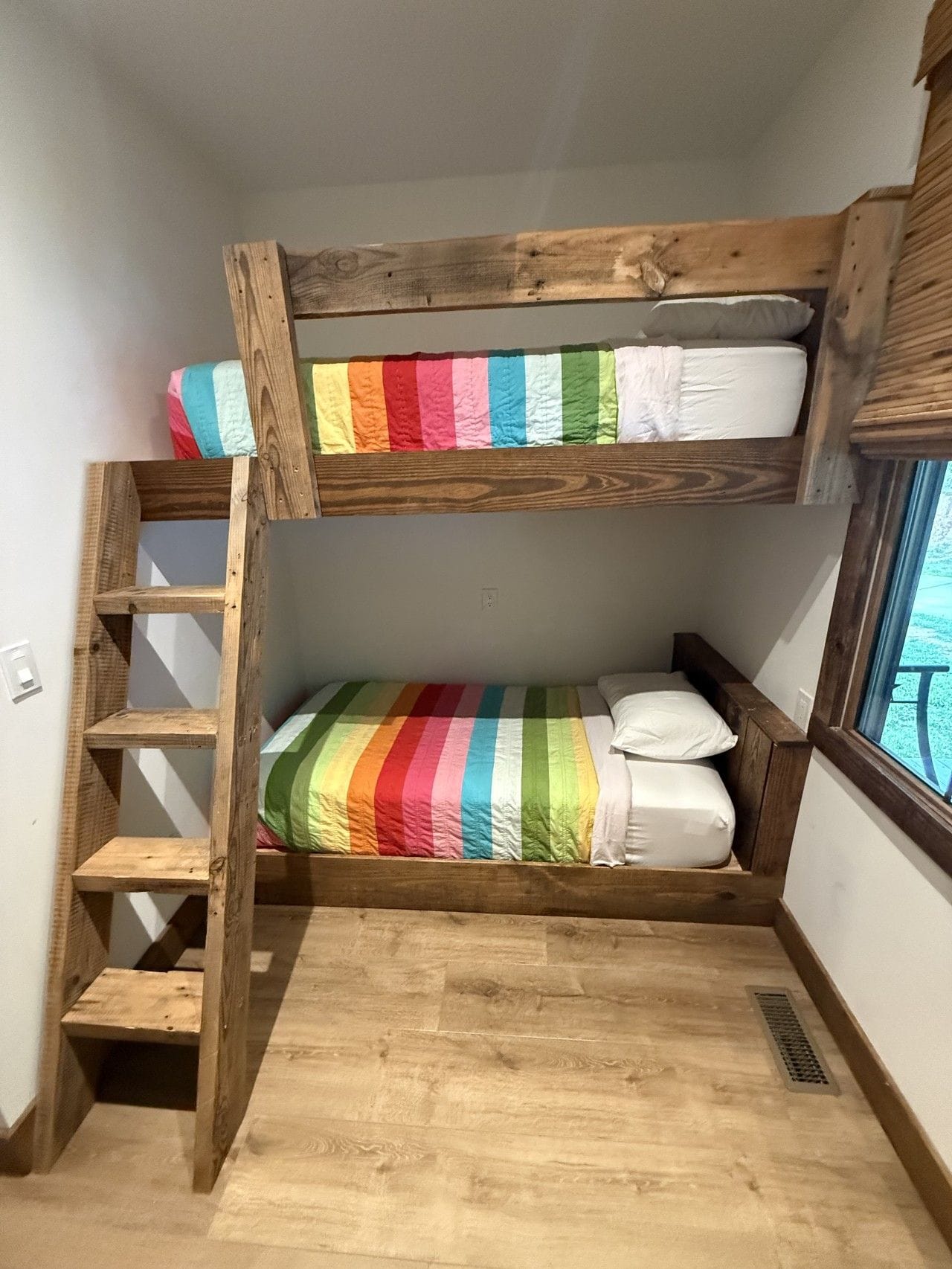 A bunk bed with a rainbow-striped bedspread and a wooden ladder.