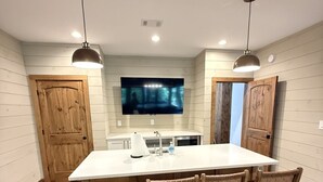 Eine geräumige Küche mit einer großen Kochinsel, Holzstühlen und einem flachbildfernseher an der Wand.
