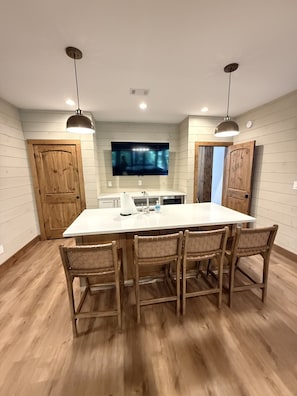 A spacious kitchen with a large island, wooden chairs, and a flat-screen TV mounted on the wall. - Luxury river home on the Chattahoochee River (Demorest)