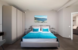 A modern bedroom with a bed, nightstands, a wardrobe, and a coastal landscape painting.