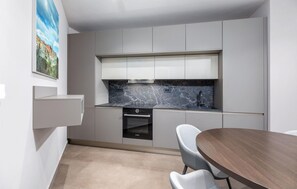 Compact kitchen with oven and microwave, adjacent dining area with round table and two chairs.