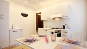 A modern kitchen with white cabinets, a dining table set with pink plates, and a cityscape clock on the wall. - Cozy apartment in Quartu Sant'Elena with WiFi (Quartu Sant'Elena)