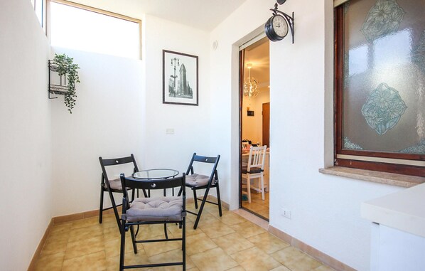 Un pequeño comedor con una mesa redonda de vidrio y cuatro sillas, un cuadro enmarcado en la pared y un ventanal con un panel de vidrio decorativo.