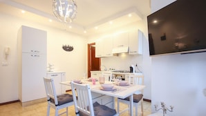 A modern kitchen with white cabinets, a dining table set for four, and a chandelier. - Cozy apartment in Quartu Sant'Elena with WiFi (Quartu Sant'Elena)
