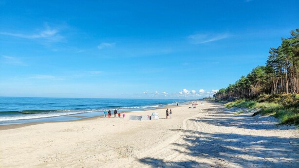 A wide sandy beach with a clear blue sky, a few people walking, and a tent set up. - 1 bedroom cozy apartment in Koszalin (Koszalin)