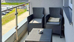A balcony with two wicker chairs and a small table, overlooking a parking area and buildings. - 1 bedroom cozy apartment in Koszalin (Koszalin)
