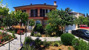 A two-story house with a balcony, surrounded by a garden with various flowers and plants. - Naomi's Sunshine (Cres)