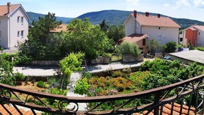 A balcony with a view of a residential area, featuring houses with red-tiled roofs and a garden with various plants. - Naomi's Sunshine (Cres)