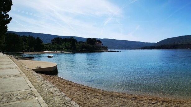 A calm lake with clear water, surrounded by mountains and a sandy beach. - Naomi's Sunshine (Cres)