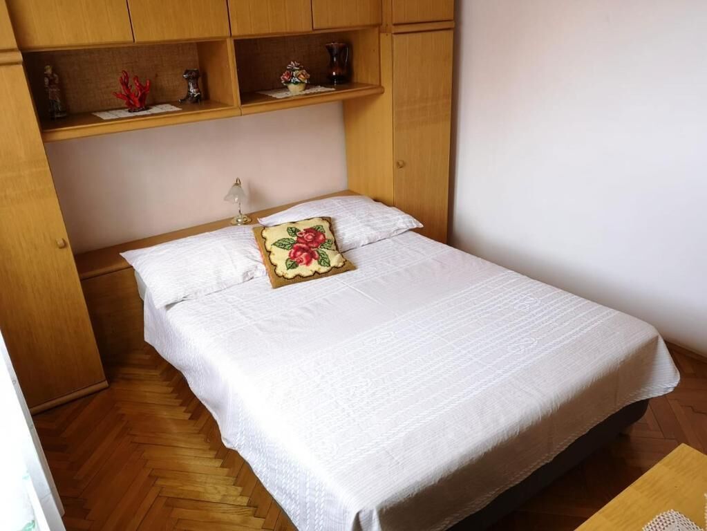 Ein Einzelbett mit weißer Bettdecke und einem Blumenkissen, ein Holzschrank und ein kleiner Tisch mit einer Vase.