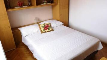 Ein Einzelbett mit weißer Bettdecke und einem Blumenkissen, ein Holzschrank und ein kleiner Tisch mit einer Vase.