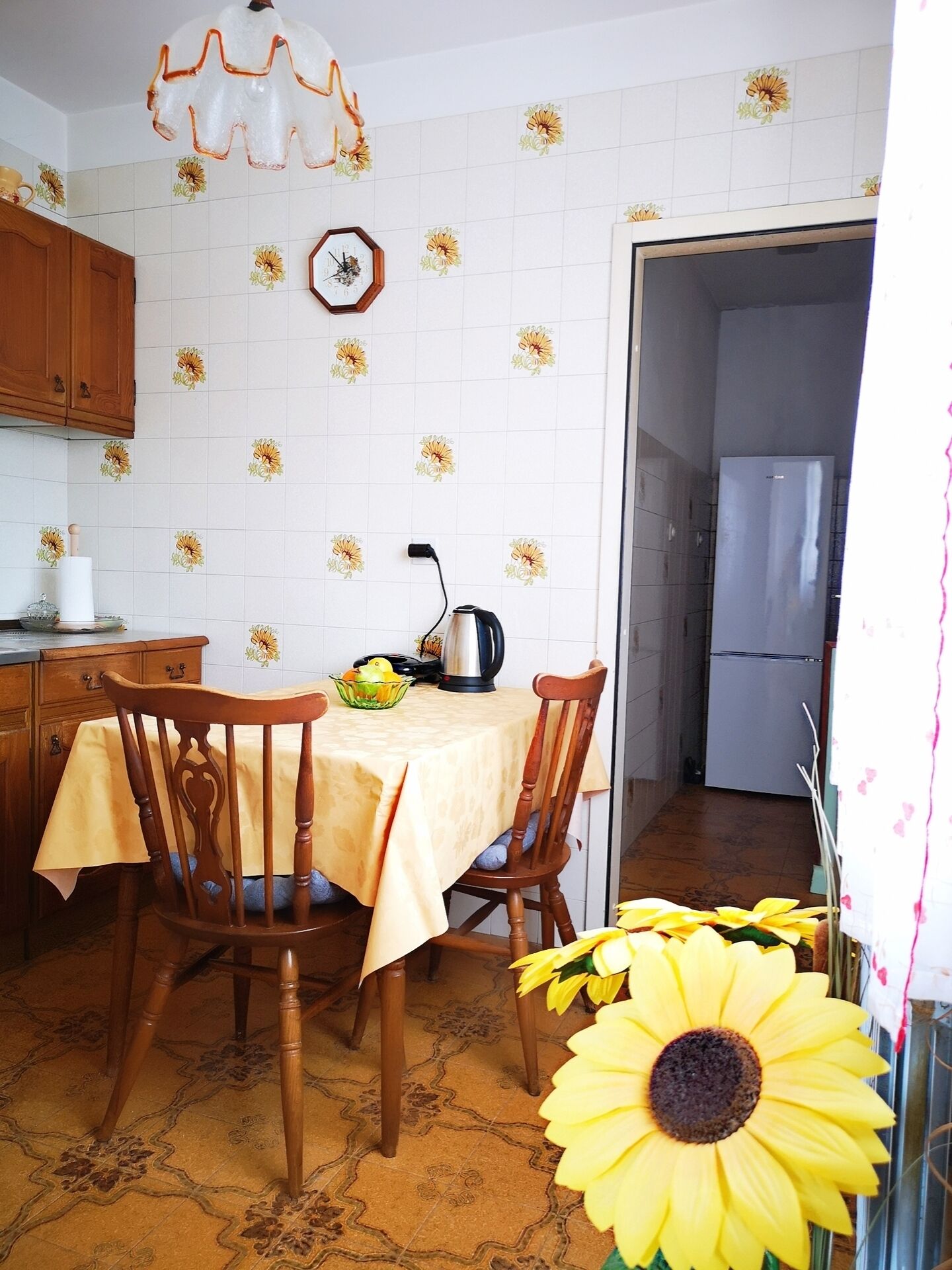 Een keuken met een eettafel, stoelen, een waterkoker en een koelkast.
