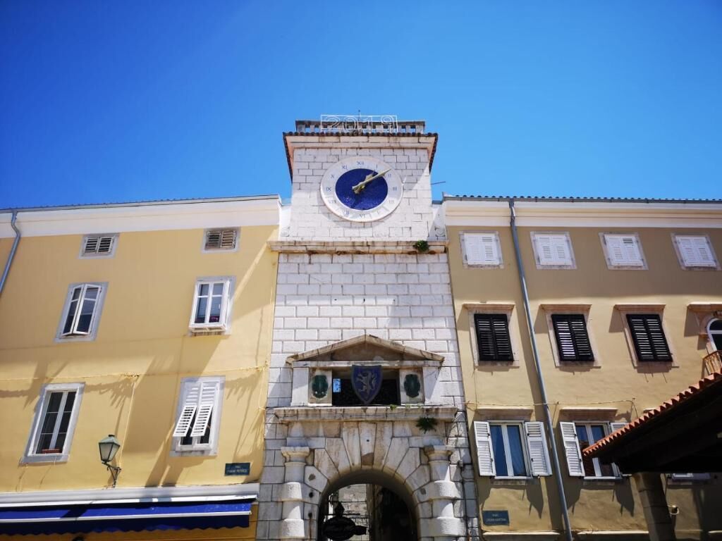 A clock tower with a blue face, set in a stone archway between two buildings.