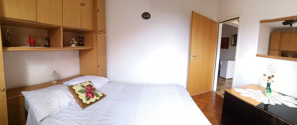 Quarto com cama, guarda-roupa de madeira e uma mesinha com um vaso.