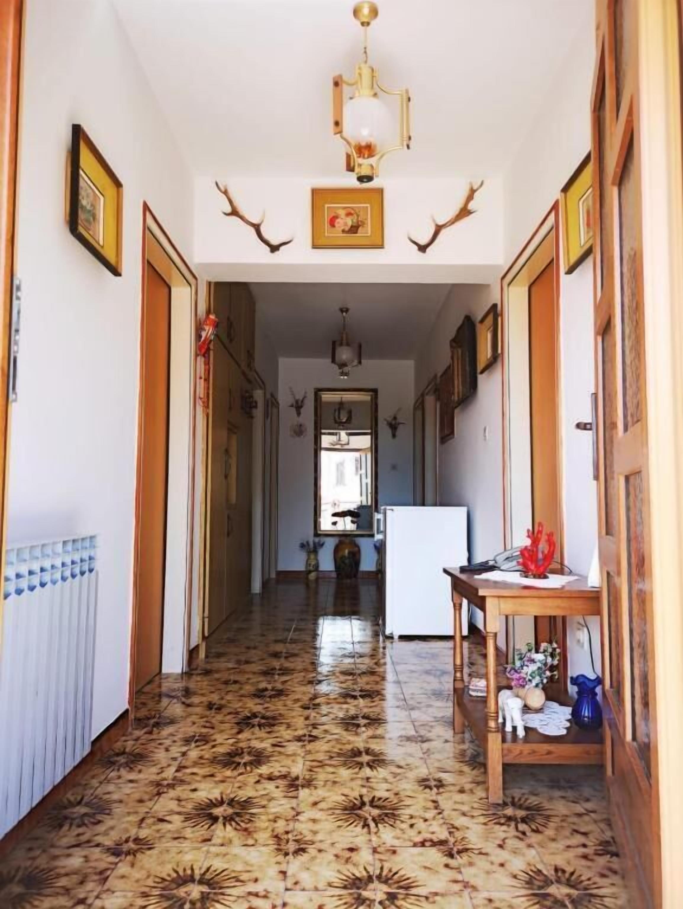 Un couloir doté d’un sol à motifs, de portes en bois et d’une table sur laquelle sont disposés divers objets.