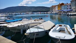 A marina with several boats docked, a clear sky, and buildings in the background. - Naomi's Sunshine (Cres)