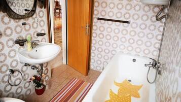 Un baño con un lavamanos blanco, un espejo, una puerta de madera, un papel tapiz estampado, una bañera con diseño de estrella de mar y un perchero.