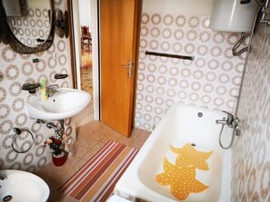 Um banheiro com pia branca, espelho, porta de madeira, parede estampada, banheira com desenho de estrela-do-mar e porta-toalhas.