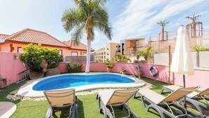 A swimming pool with lounge chairs, a palm tree, and a pink wall. - Nice 3 Bedroom Villa in El Duque  (Costa Adeje)