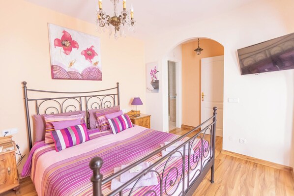 Une chambre à coucher comprenant un lit, une table de chevet, une lampe, un tableau et une porte donnant sur une autre pièce.