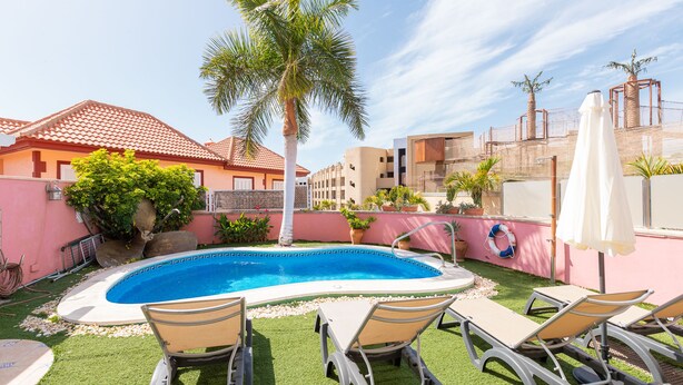 A swimming pool with lounge chairs, palm trees, and a pink wall. - Nice 3 Bedroom Villa in El Duque  (Costa Adeje)