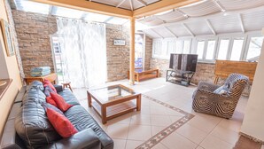 A spacious living room with a stone wall, a black leather sofa, a wooden coffee table, and a zebra-patterned chair. - Nice 3 Bedroom Villa in El Duque  (Costa Adeje)