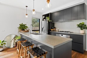 A modern kitchen with a central island, dark cabinetry, and pendant lighting. - McMillan Escape (Anglesea)